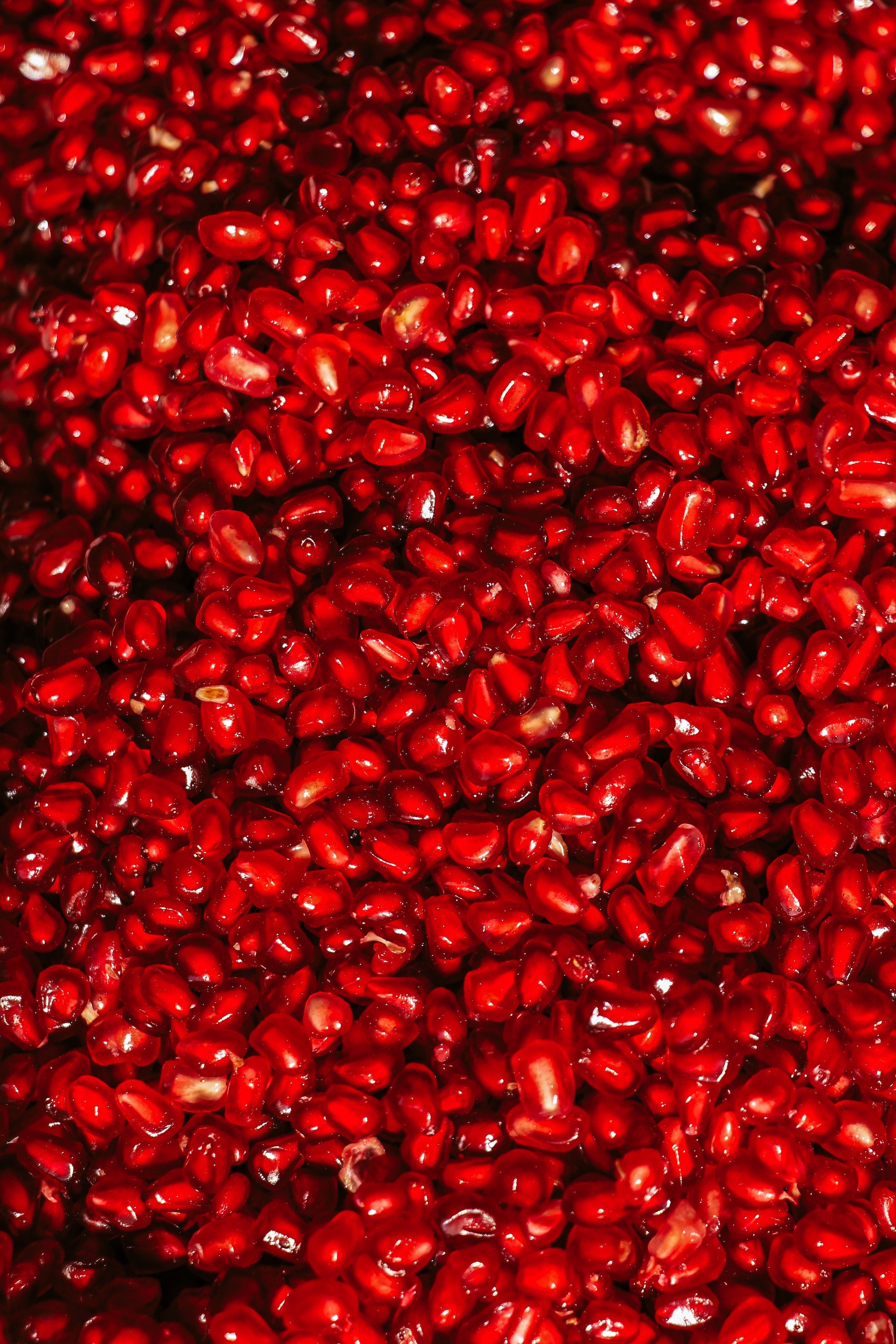 Description: A close-up photograph of a ripe pomegranate, showcasing its vibrant red color and textured outer skin. The pomegranate is split open to reveal its juicy, ruby-red seeds inside.